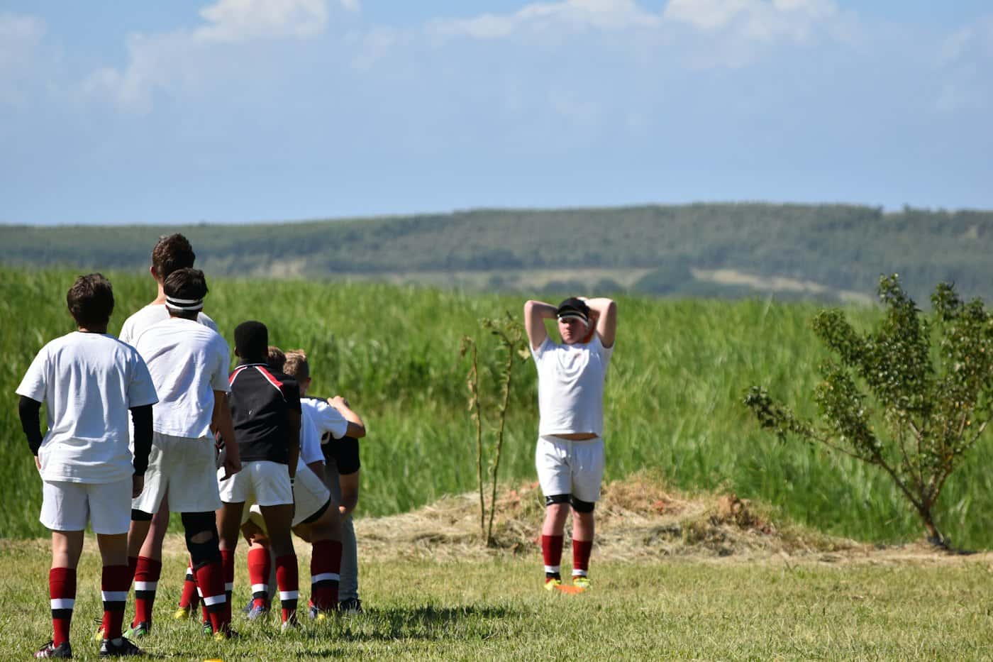 Un gruppo di giocatori in divisa bianca osserva l'allenamento a bordo campo, di spalle